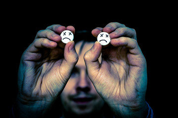 Fototapeta premium The man is holding two large white pills. On tablets drawn emoticons.