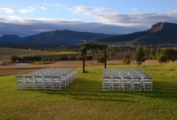 Idyllic wedding scene set out with white chairs and a floral arch overlooking the mountains and...
