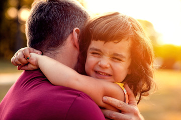 Fototapeta premium Portrait of father holding daughter in his hands and hugging each other outdoors.