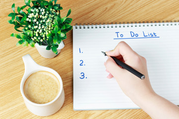 Female hand writes To Do List in a notebook on wooden table, planning concept