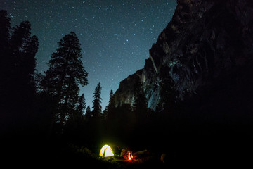 campfire under night sky with star on top of mountain surrounded by forest