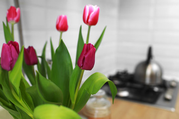 Tulips bouquet close up at home standing on a wooden countertop in the kitchen. Modern white u-shaped kitchen in scandinavian style. Open shelves in the kitchen with plants and jars.
