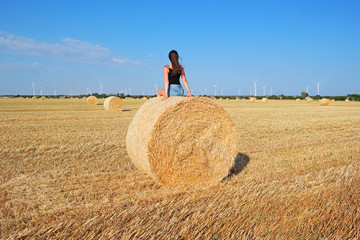 Naklejka na ściany i meble Girl on a haystack in a field with blue sky