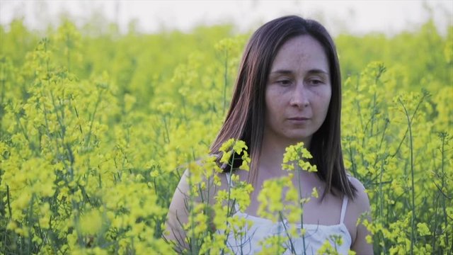 A beautiful woman with dark hair and freckles on her face walks in a large rapeseed field in the summer, moths fly around. Girl enjoying nature