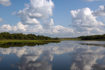 Clouds are reflected in the river. A small technological bridge, device for water discharge.  Beautiful river landscape. Reflection of clouds in water. The surface of the water