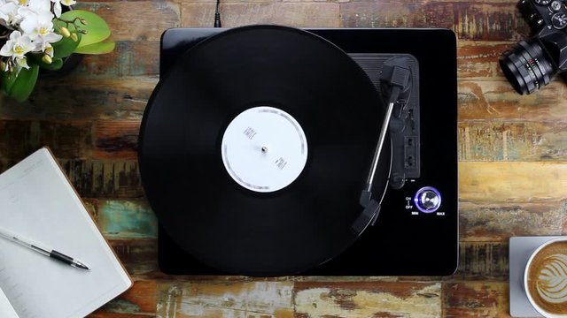 Vinyl Record Player Turntable on a Stylish Wood Table with Notepad, Camera, Orchid Flower and Coffee - Birdseye View Top Shot Static