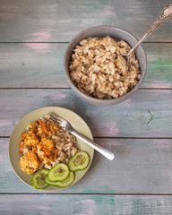 Home meal of barley porridge, chicken stew and slices of cucumbers in two plates