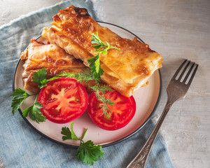 Plate with baked homemade sandwiches and halves of red tomato and fork on a blue napkin