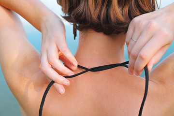 Female swimmer ties up her bikini near the water. Close-up view of a woman from her back on the...