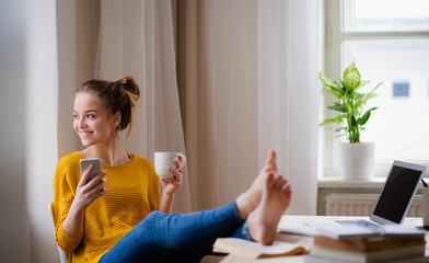 A young female student sitting at the table, using smartpone when studying.
