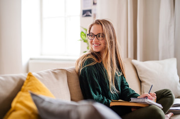 A happy young female student sitting on sofa, studying.