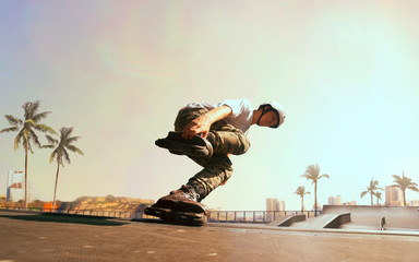 Rollerskater man is performing tricks in skatepark on sunset.