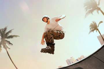 Rollerskater man is performing tricks in skatepark on sunset.