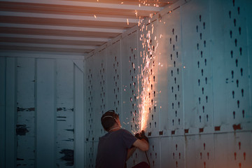 A worker inside an iron container polishes metal. Sparks fly from friction