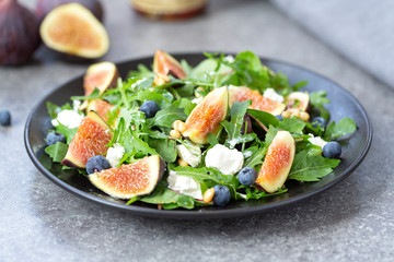 Fig salad with goat cheese, blueberry, with pine nuts and arugula on grey background. Healthy food. Vegetarian food. Close up