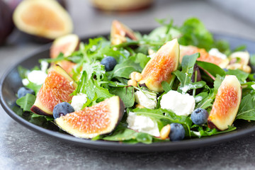 Fig salad with goat cheese, blueberry, with pine nuts and arugula on grey background. Healthy food. Vegetarian food. Close up
