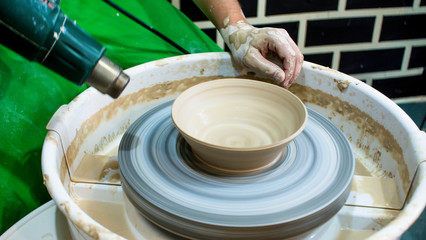 A raw clay pot in the hands of a potter. Workshop in the pottery workshop. Clay pot on a potter`s wheel