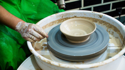 A raw clay pot in the hands of a potter. Workshop in the pottery workshop. Clay pot on a potter`s wheel