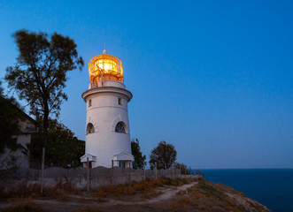 Naklejka premium White sea lighthouse in Feodosia, Crimea on the Black Sea from the light under the evening sky