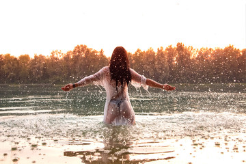 Frau in weißem Kleid steht in See, Sonnenuntergang