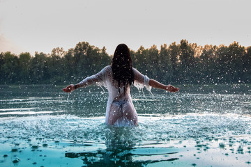 Frau in weißem Kleid steht in See, Sonnenuntergang
