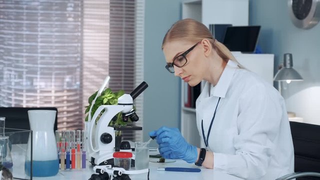 Female chemistry professor in lab coat using pipette to drop fertilizers on something and doing that two times