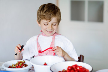 Little blond kid boy helping and making strawberry jam in summer