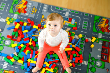 Adorable baby girl playing with educational toys . Happy healthy child having fun with colorful different wooden blocks at home in domestic room. Baby learning colors and forms