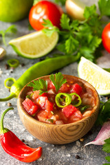 Traditional Latin American mexican salsa sauce with ingredients on a light stone table.