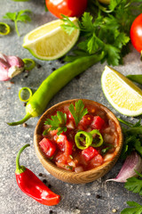 Traditional Latin American mexican salsa sauce with ingredients on a light stone table.