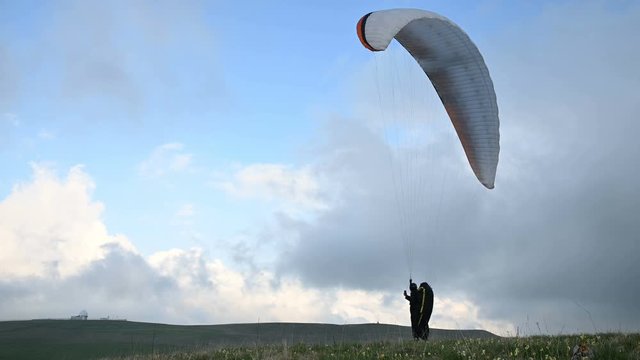 A male athlete paraglider raises a wing in an outdor against the backdrop of evening clouds but cannot fly. Failure while trying to take off