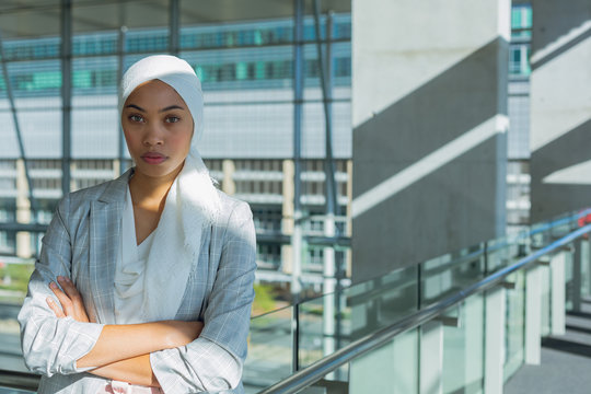 Businesswoman in hijab with arms crossed looking at camera in corridor at modern office