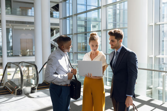 Young business people stand using laptop in modern office lobby