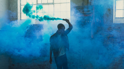 Young man holding smoke bomb in empty warehouse