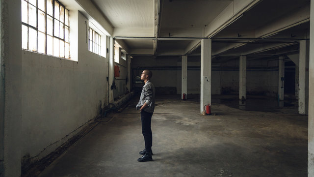 Side view of young man standing in empty warehouse