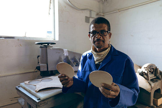 Portrait of a middle aged man holding leather cut outs at a sports equipment factory