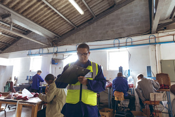 Young man writing on a clipboard in a cricket ball factory