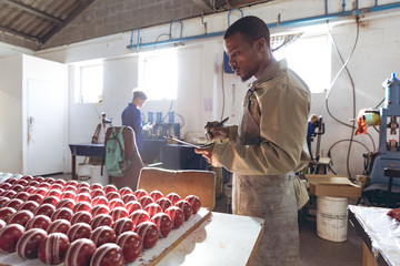 Young man holding a clipboard in a cricket ball factory