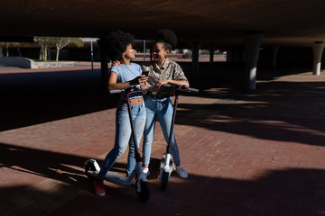 Two young women riding e scooters