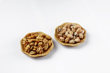 wood plates of salted peanuts and pistachios on white background. snack to beer