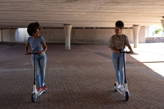 Two young women riding e scooters - Powered by Adobe