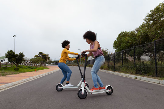 Young women riding e scooters in the street - Powered by Adobe