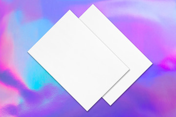 Two empty white rectangle poster mockups lying diagonally on top of each other with soft shadows on holographic background. Flat lay, top view