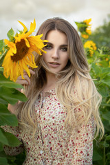 Close-up portrait of a blond girl in a summer simple dress among sunflowers close-up