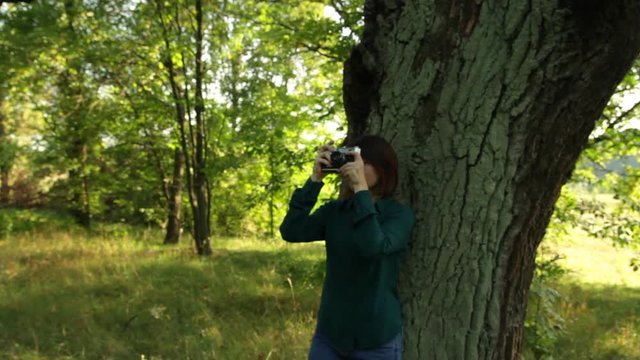 Girl with an old-fashioned camera walks in a forest. A young woman taking photos.