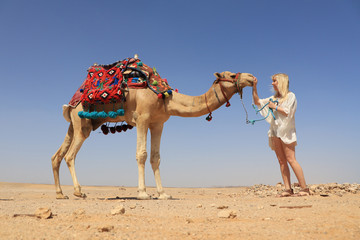 eine blonde Frau streichelt ihr Kamel in der Wüste