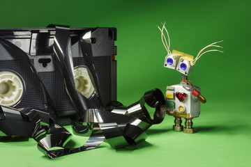 Funny robot-cyborg with VHS video tapes and film on a green background. 