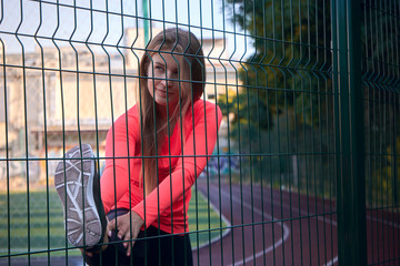 A beautiful and athletic woman stretches her elbowed legs on a fence.