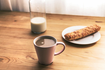 Morning breakfast: coffee, puff pastry cake and bottle of milk on a wooden table, soft focus