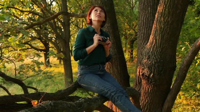 Girl with an old-fashioned camera walks in a forest. A young woman taking photos.
